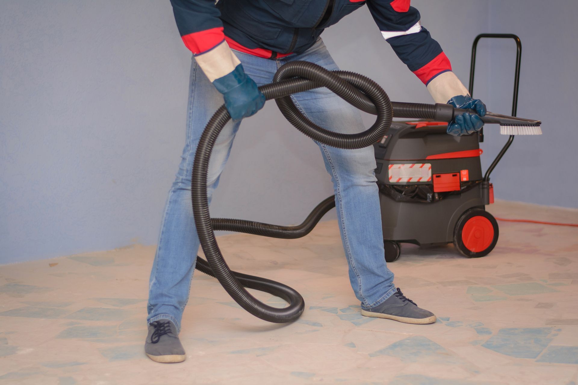a cleaner in special clothes and rubber gloves holds a knot of corrugated hose from an industrial vacuum cleaner. Cleaning services rooms